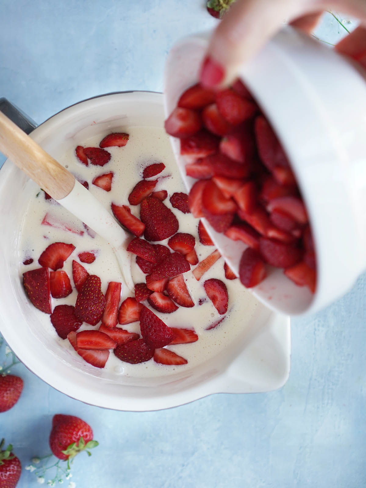 Pouring sliced strawberries from a bowl into a large bowl with the cream.