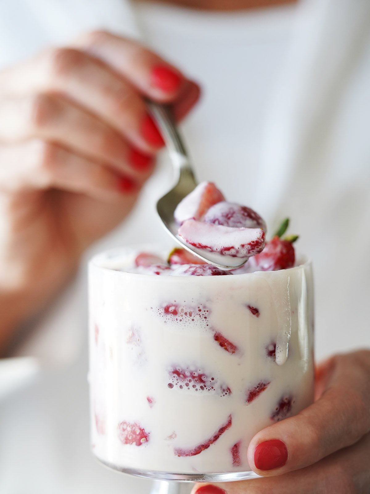A hand holding a glass cup with fresas con crema.