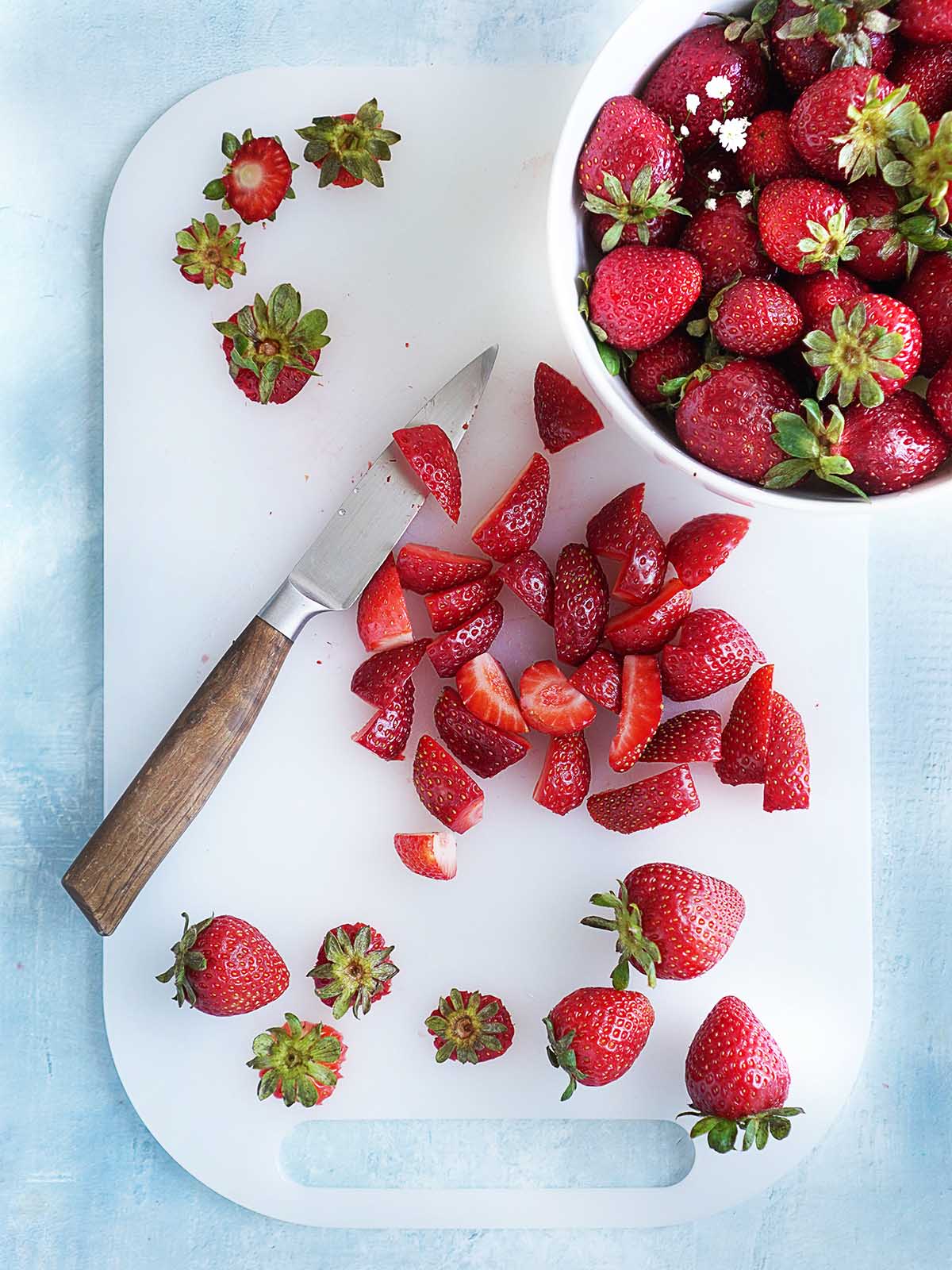 Slicing strawberries on a white cutting board.
