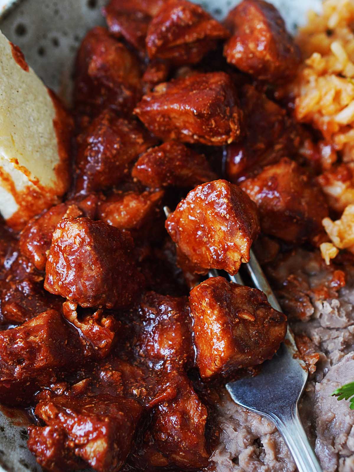 Close up image cooked pork cubes covered in red sauce.