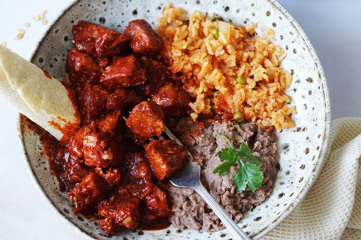 A wide bowl with carne con chile, rice and beans on the side.