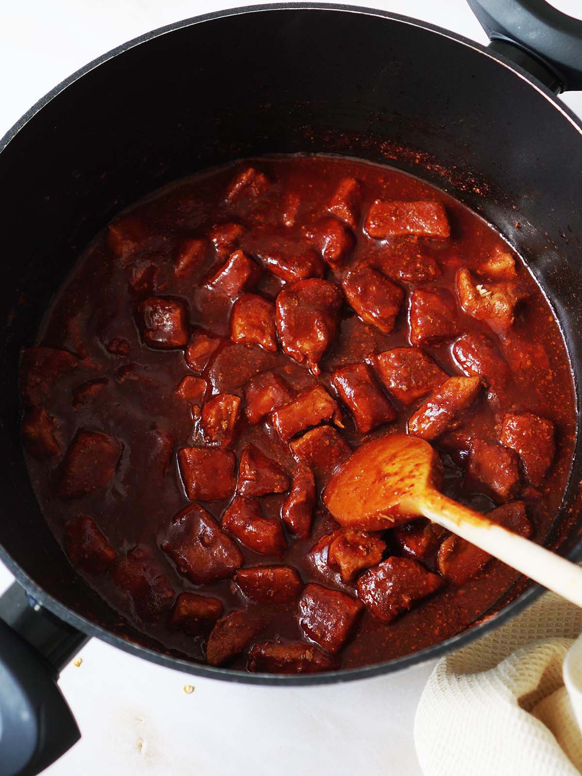 Cooking cubes of pork in a red sauce inside a large sauce pot.