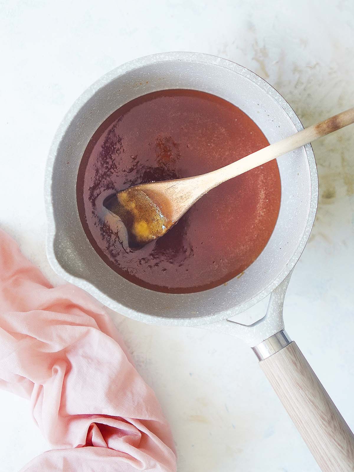Caramel sauce in a sauce pot with a wooden spoon.