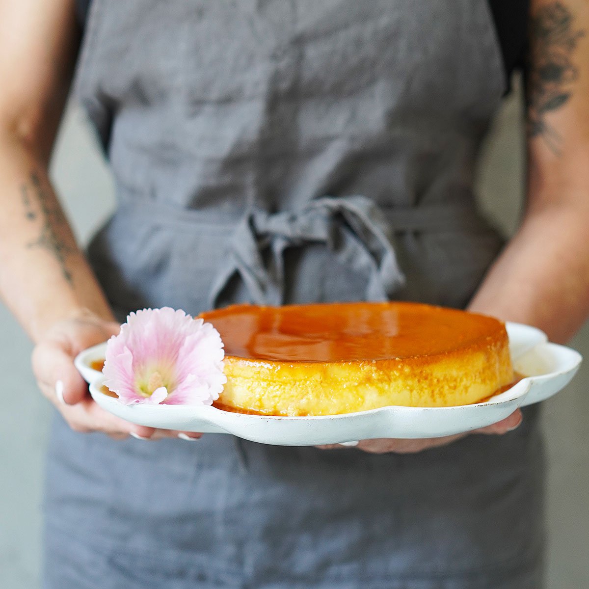 A person holding a flan placed in a serving plate with a pink flower on the side.