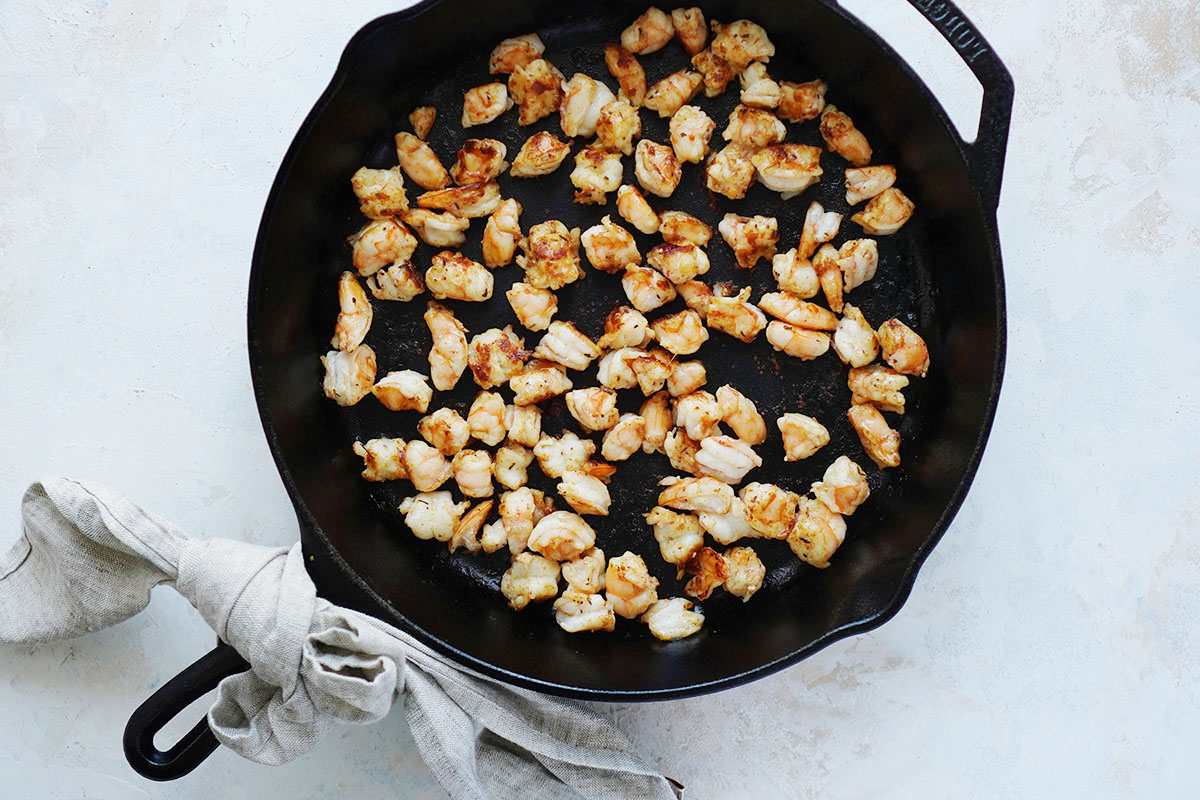 An iron skillet with pieces of cooked shrimp.