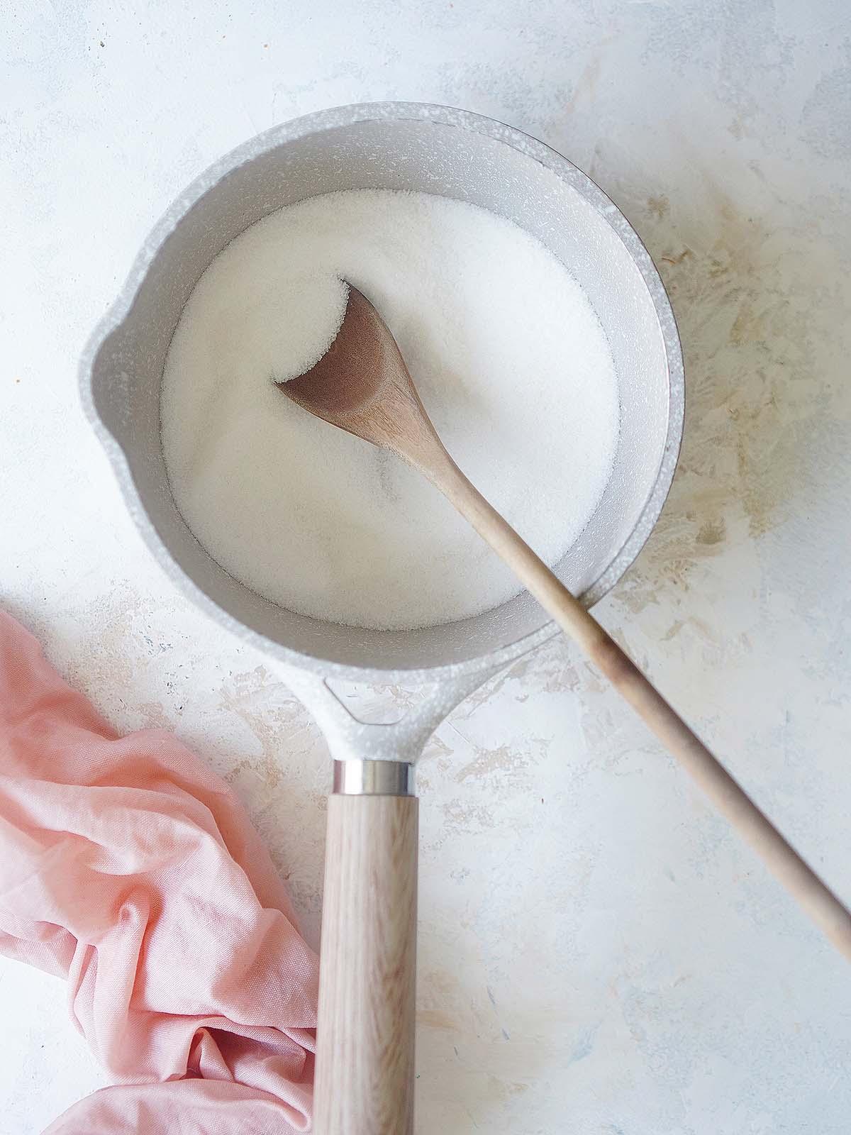 Sugar placed inside a sauce pan and a wooden spoon.