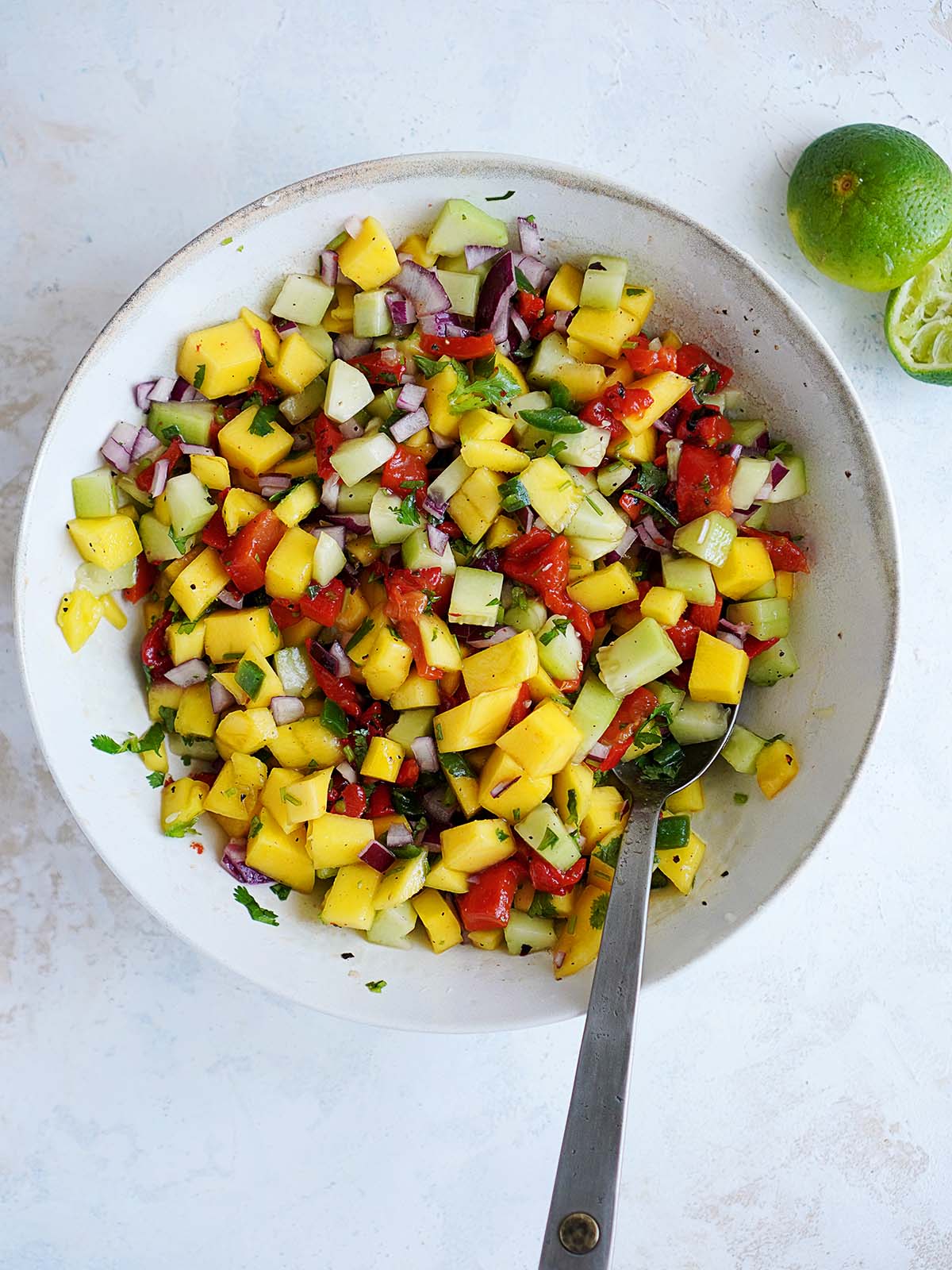 A bowl with mango salsa and a spoon.