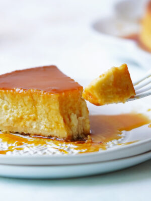 A slice of flan on a white plate with a fork taking a piece.