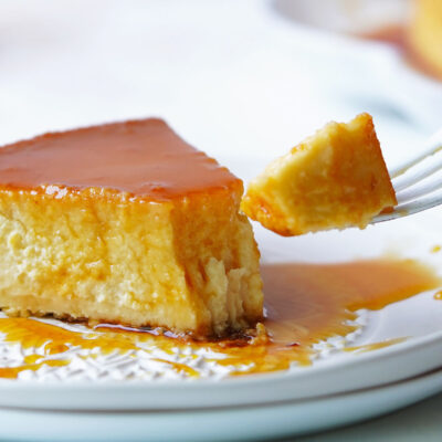 A slice of flan on a white plate with a fork taking a piece.