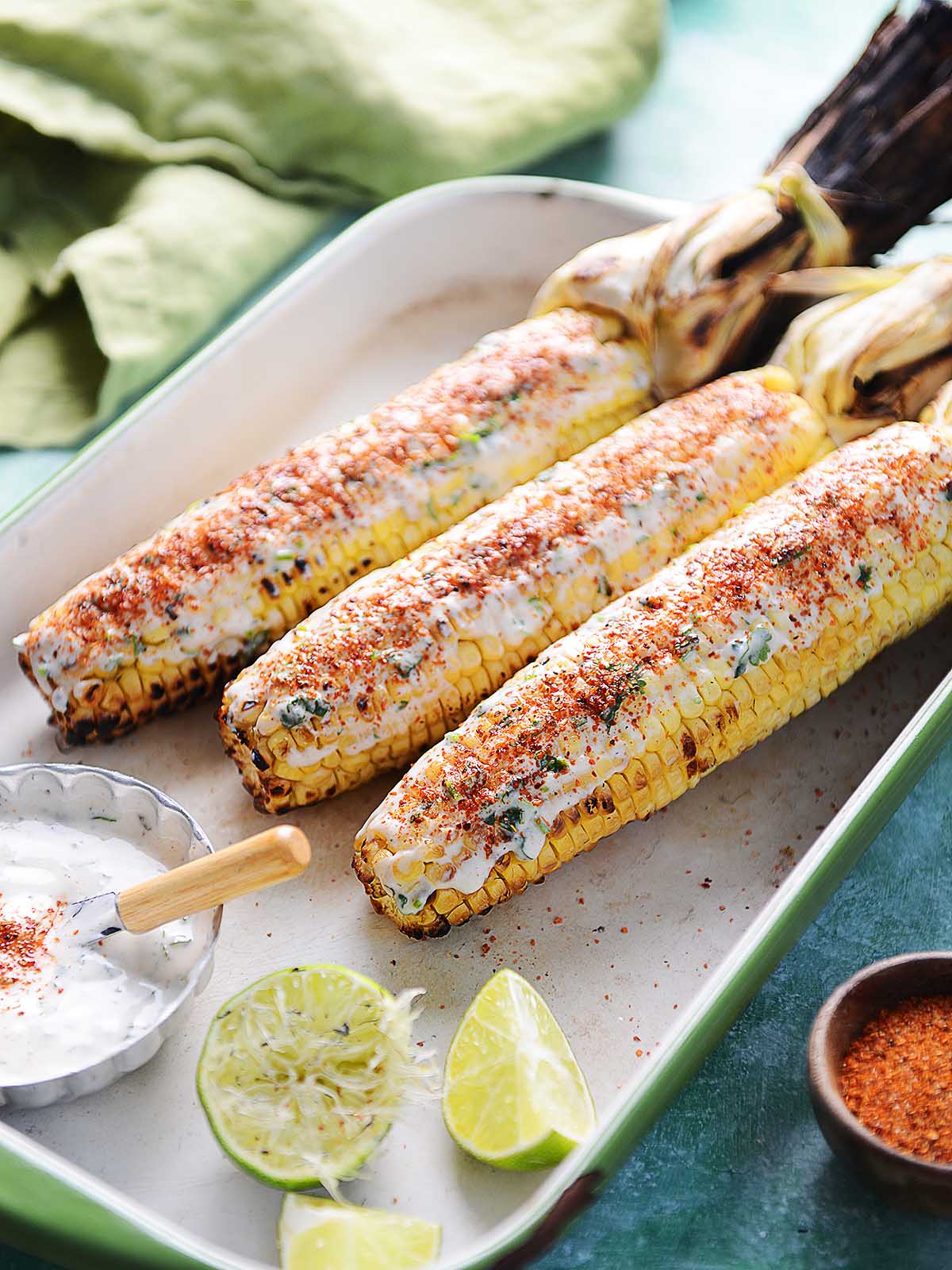 Three Elote Asado with the husk pulled back and crema on top of the corn.