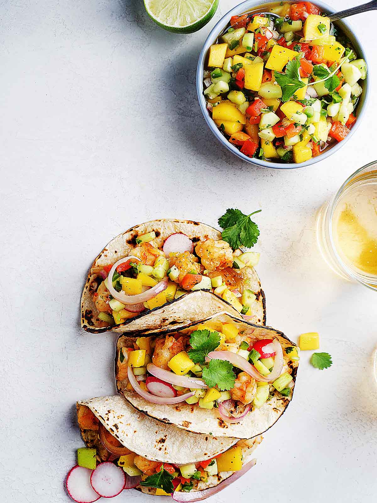 Three shrimp tacos with mango salsa made with corn tortilla and a lime slice on the side.