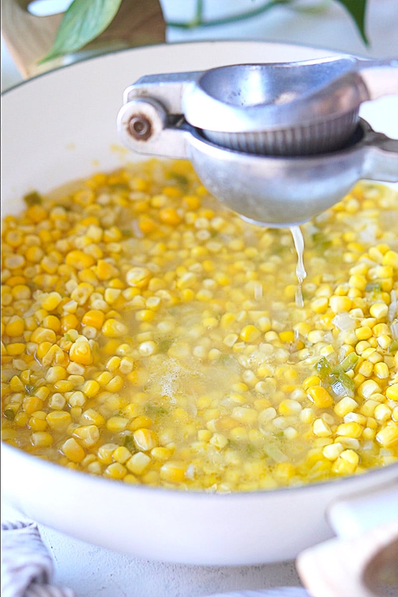 A lime squeezer pouring lime juice to a skillet with corn kernels.