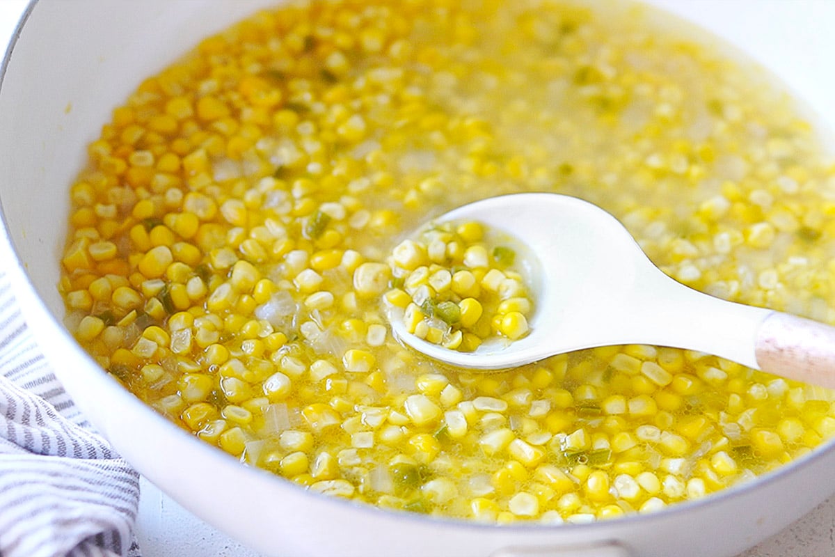 A white skillet with cooked corn kernels.