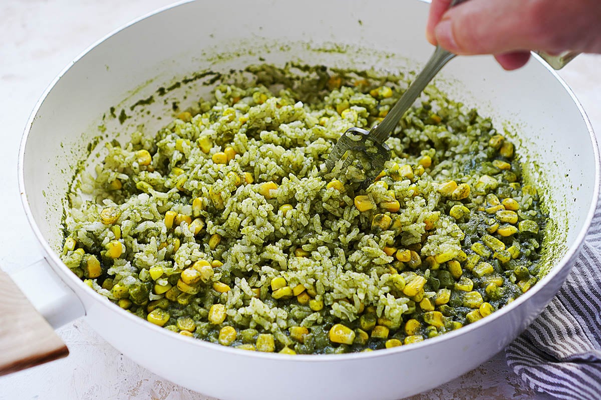 A white pot with a fork fluffing the green rice, corn kernels.