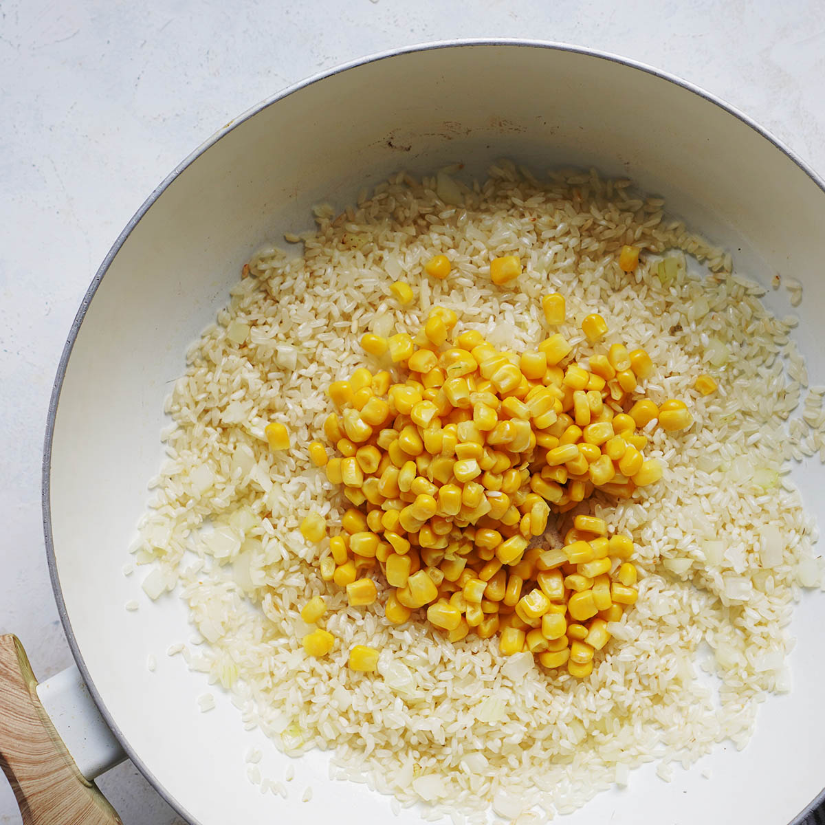 A white pot with sauteed white rice and corn kernels.
