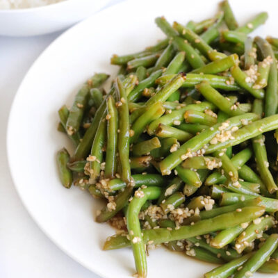 Cooked green beans on covered with garlic and sesame seeds on a white plate.