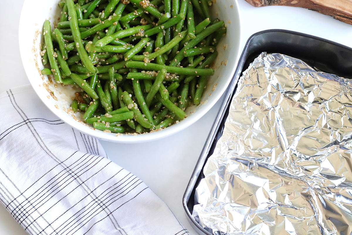 A baking tray lined with foil and the green beans on the side in a bowl.