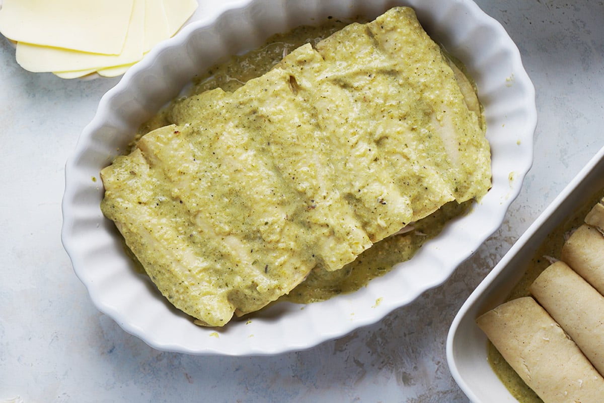 A white oval baking dish with prepared green enchiladas.