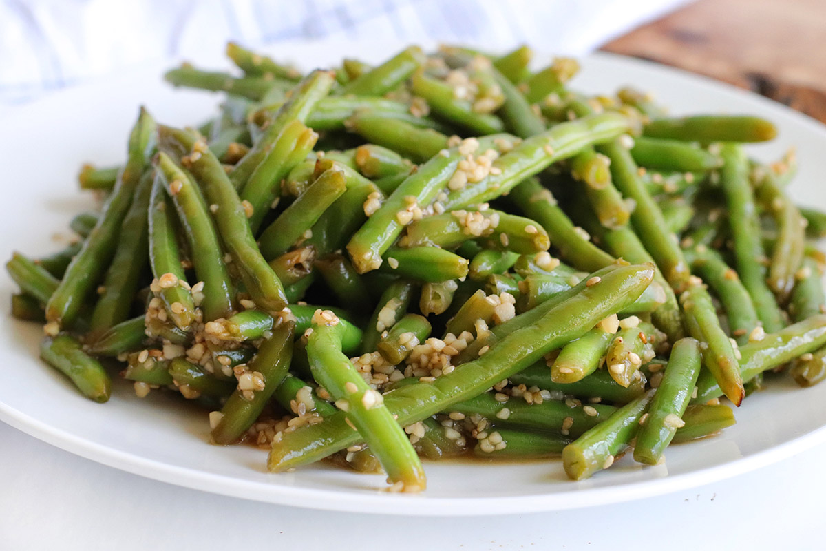 A white plate with green beans covered with chopped garlic in a sesame sauce.