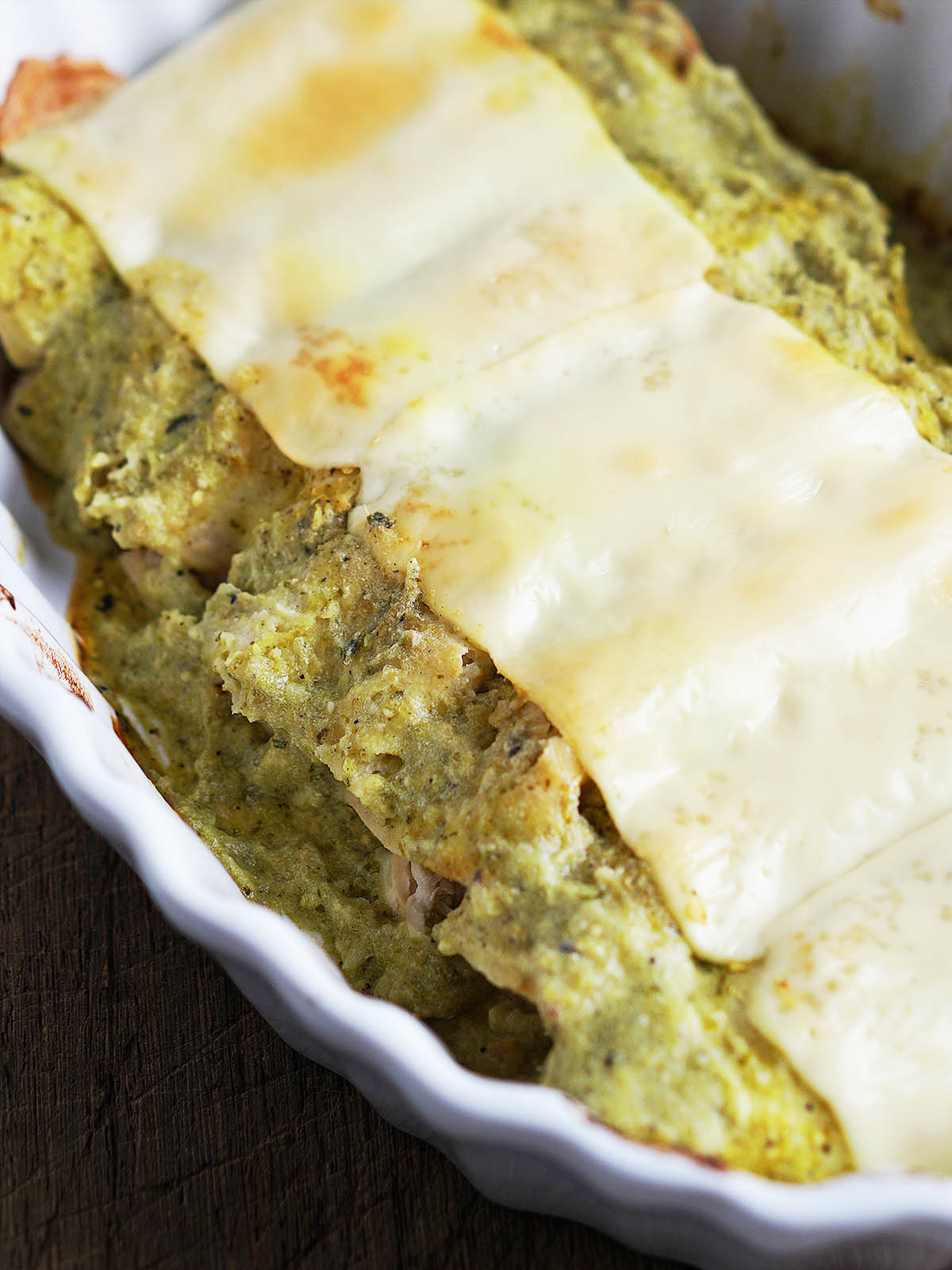 A white oval baking dish with cooked green enchiladas.