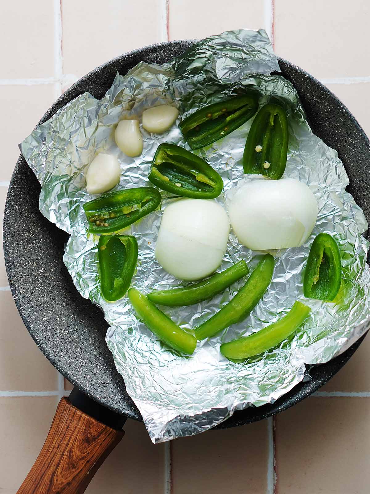 A gray skillet with raw white onion, jalapeños, serrano peppers and garlic.