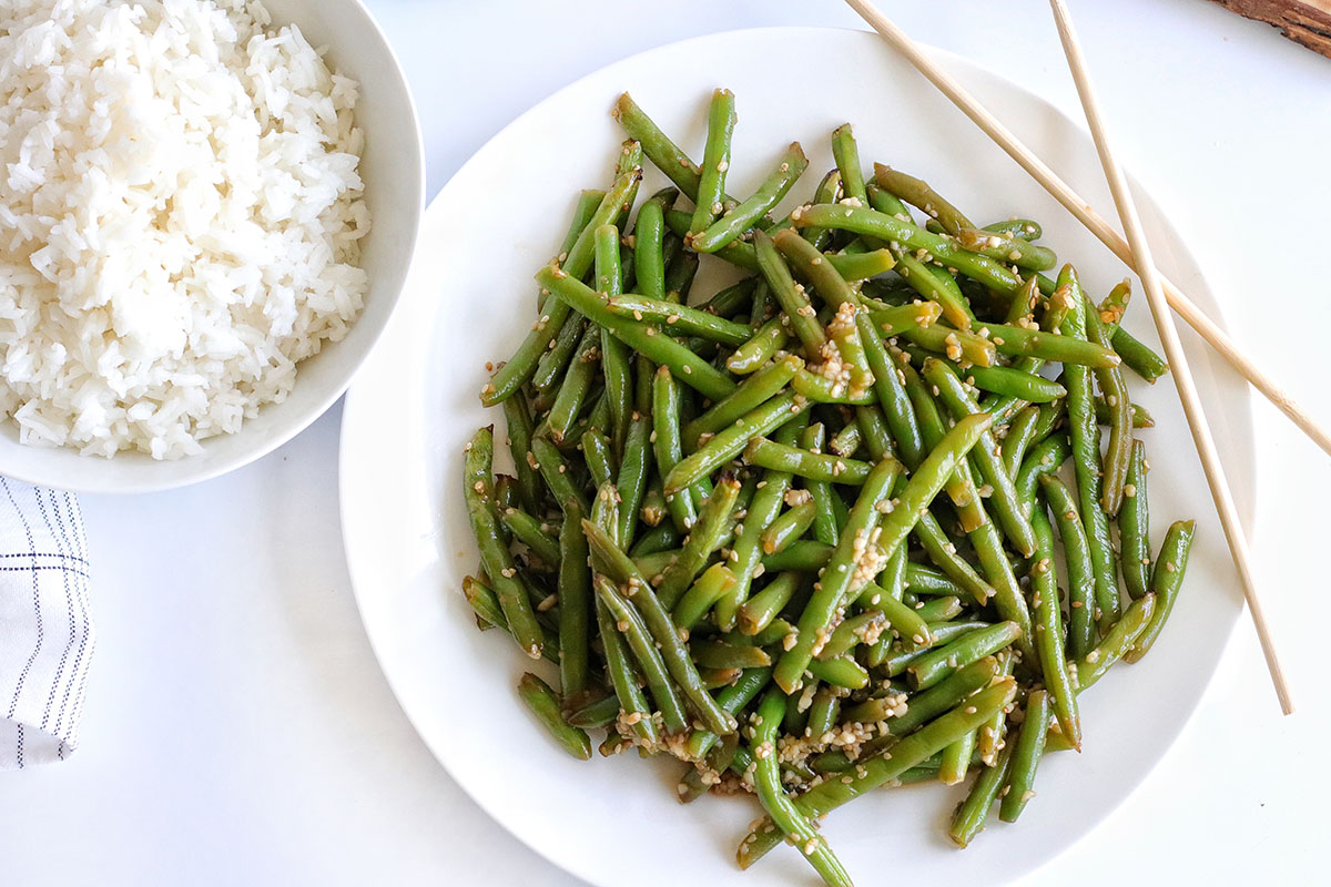 Air Fryer Frozen Green Beans on a white plate with chopsticks and white rice on the side.