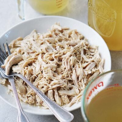 A white bowl with shredded chicken and two forks on the side.