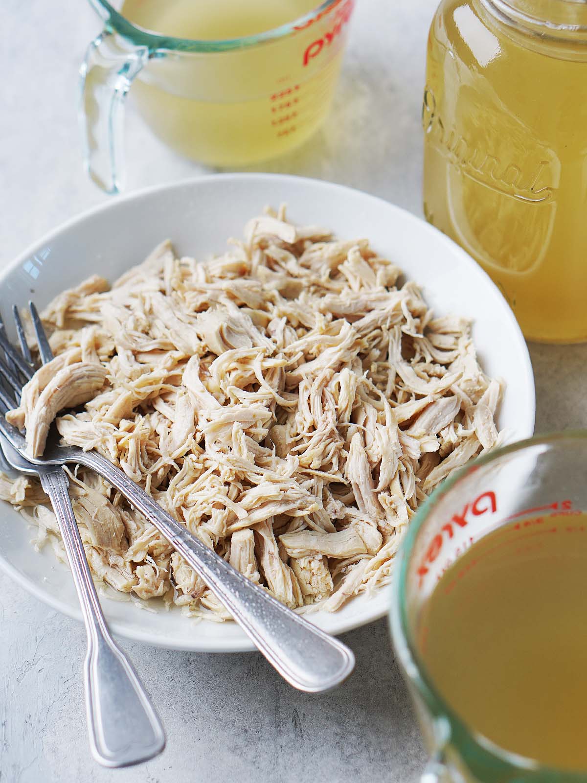 A white bowl with shredded chicken and two forks on the side.