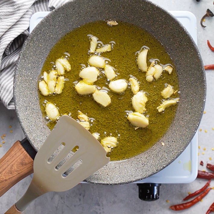 A gray skillet sauteing garlic cloves in olive oil.