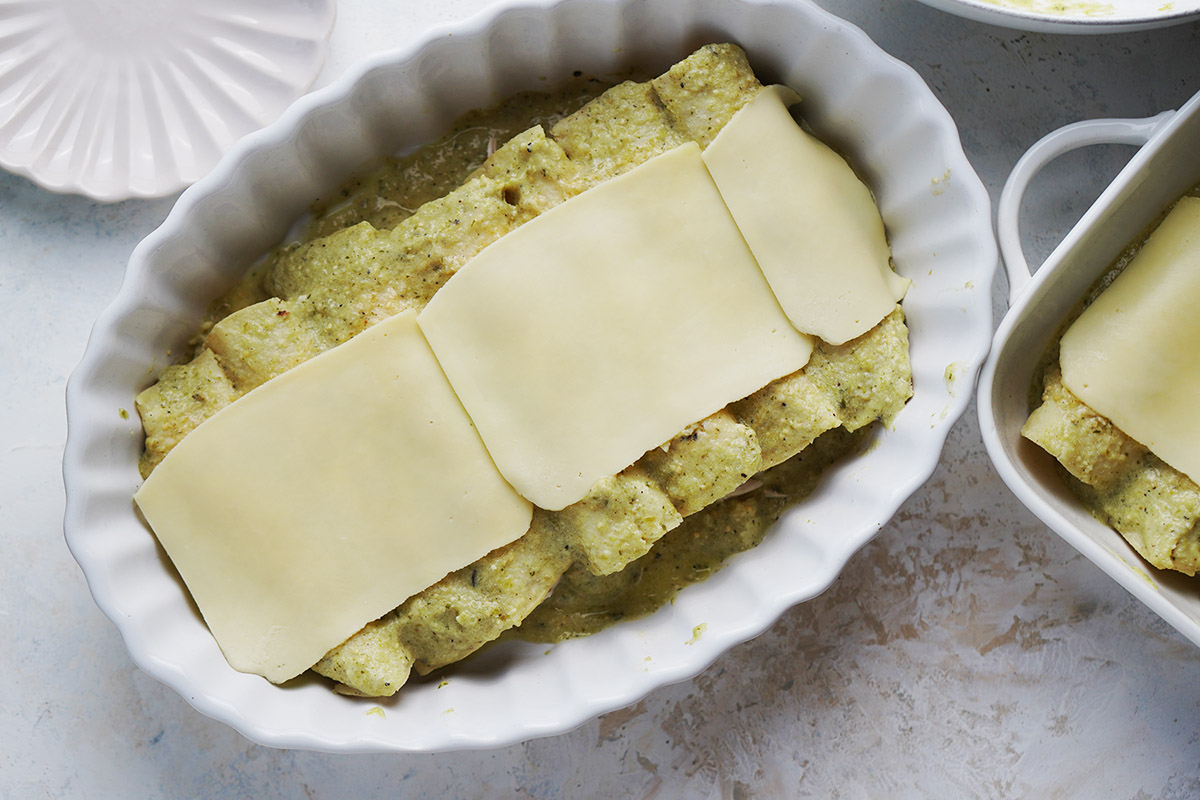 A white oval baking dish with prepared green enchiladas.