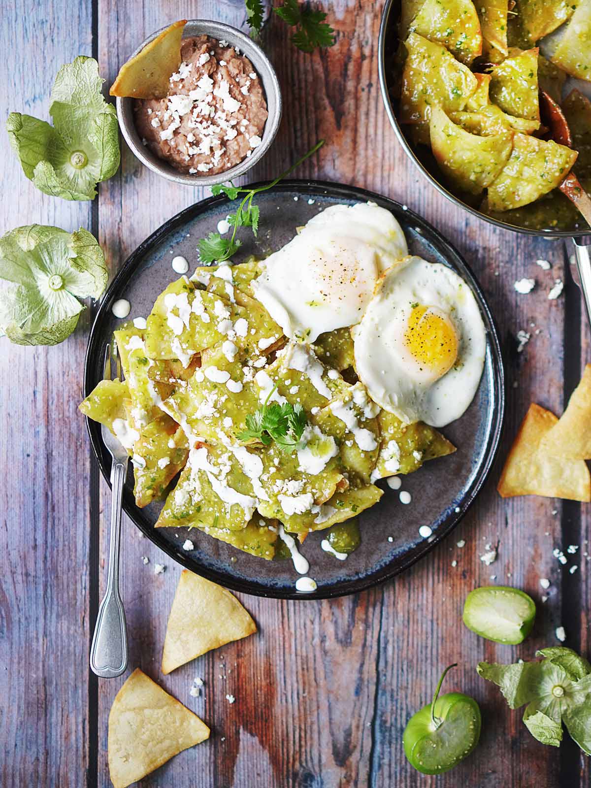 A plate with chilaquiles drizzled with mexican crema and two sunny side up eggs on the side.