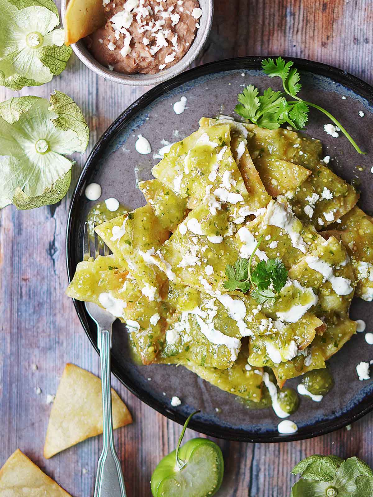 A plate with chilaquiles verdes drizzled with mexican crema and garnished with a cilantro sprig.