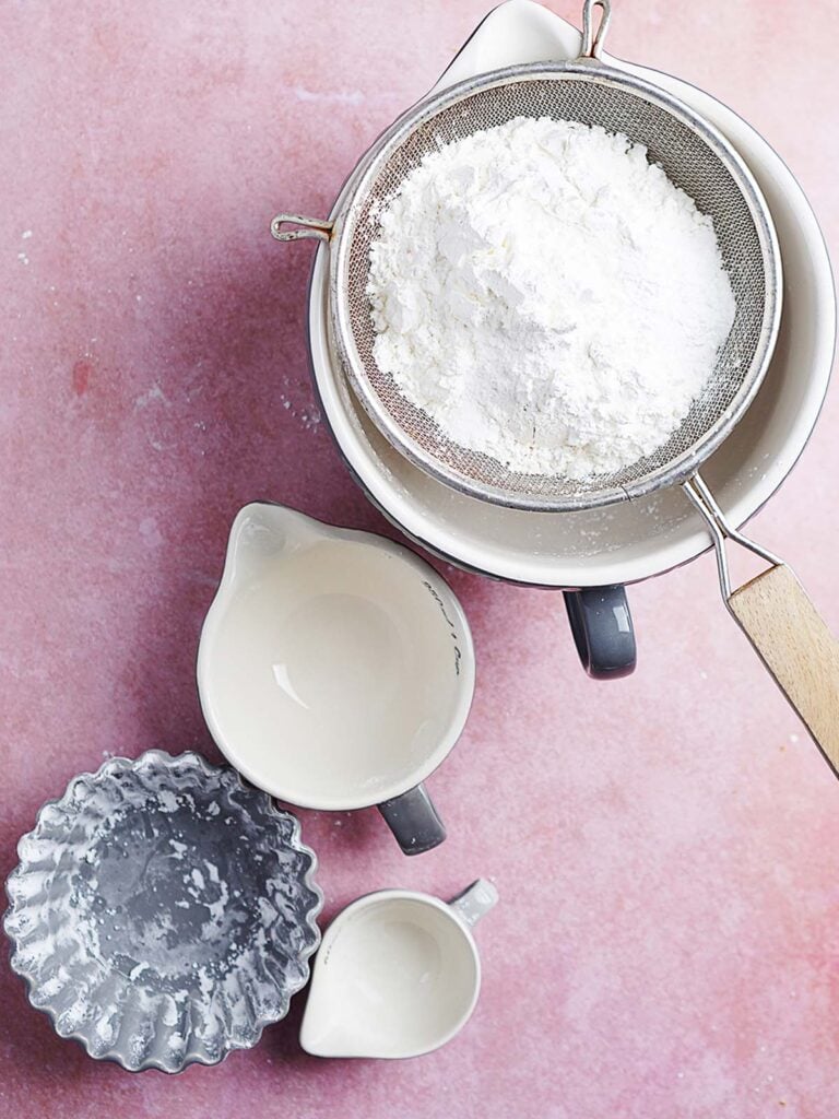 Sifting flour thru a mesh colander over a mixing bowl.