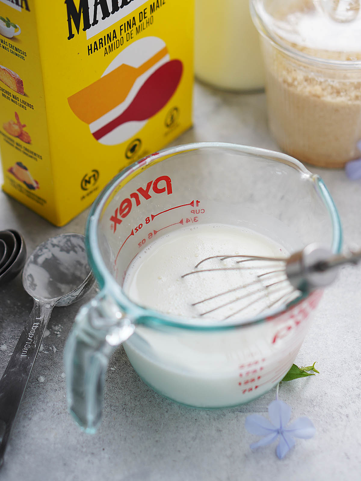 Mixing cornstarch with milk in a measuring cup, a box of Maizena in the background.