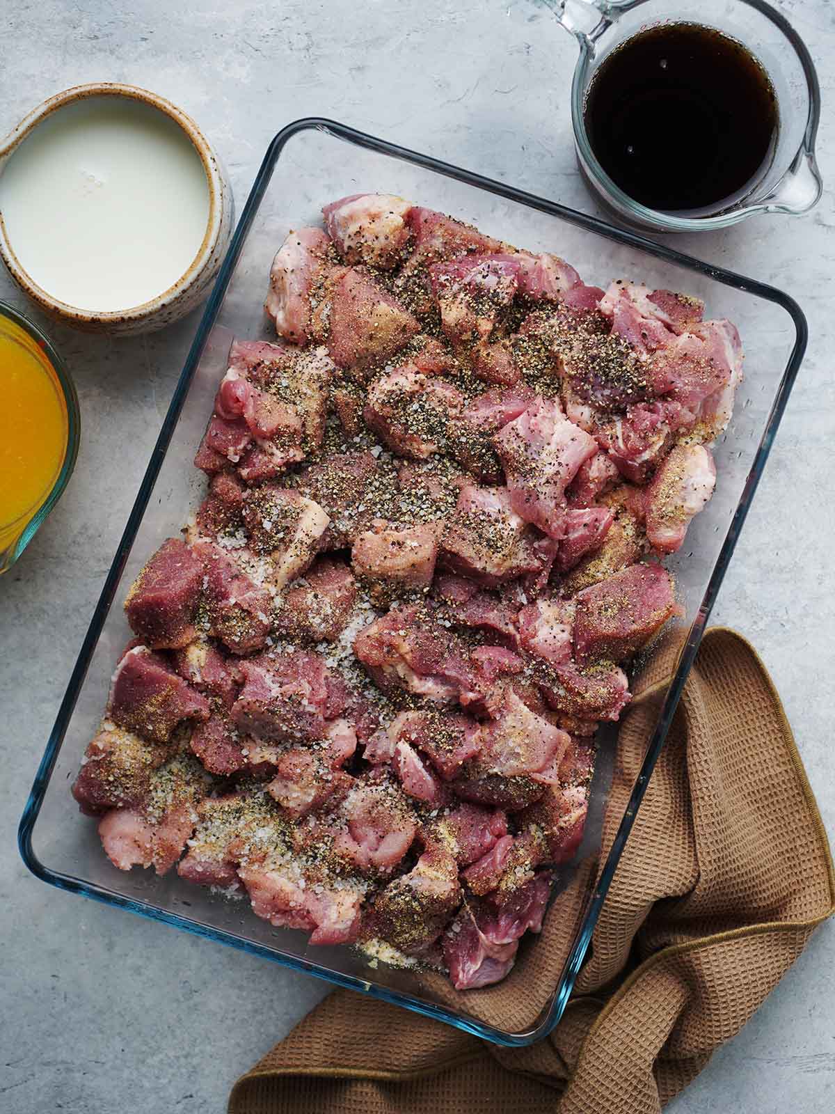Raw pork chunks placed in a baking dish with seasoning.