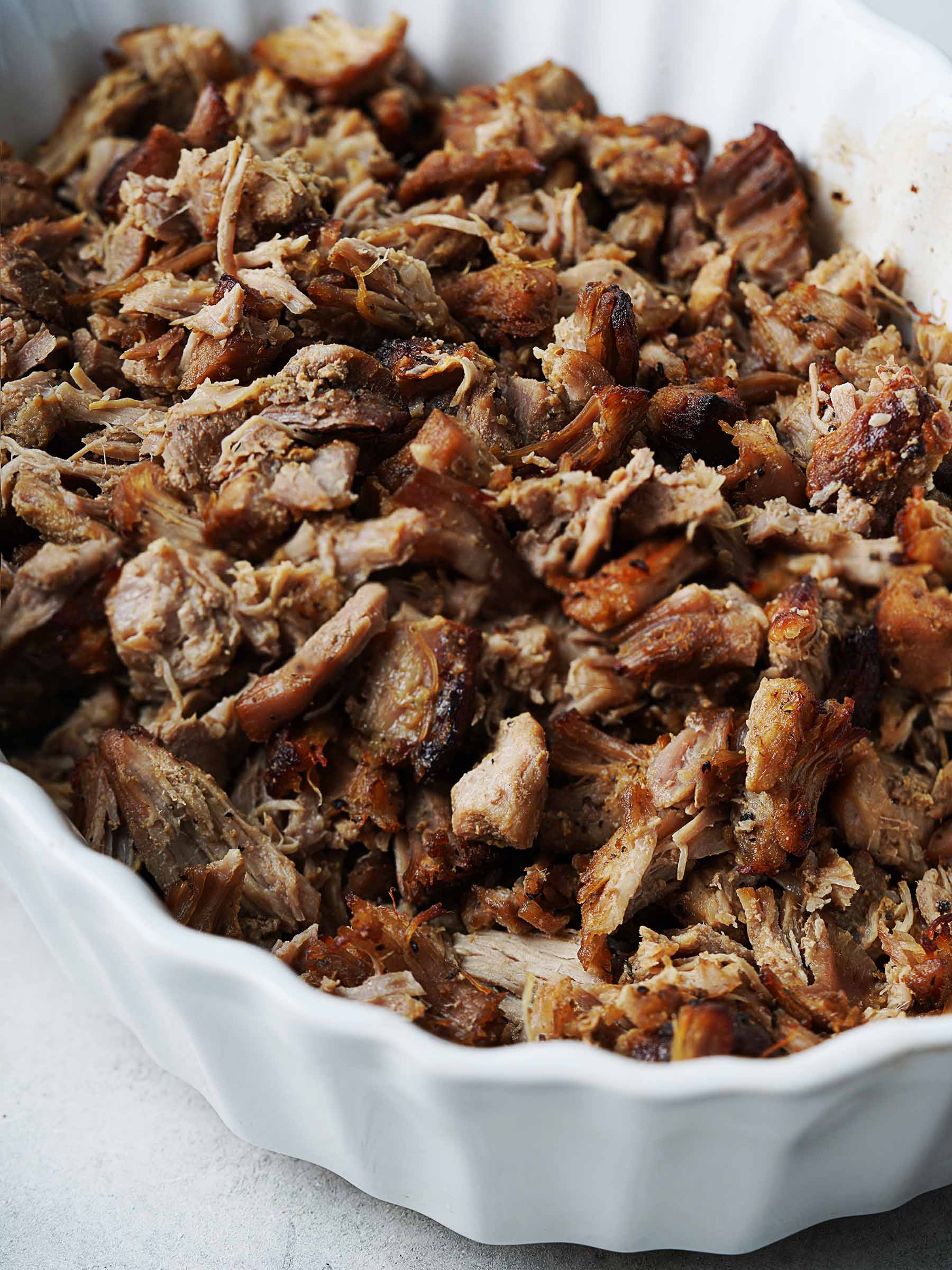 Cooked crispy pulled pork inside a white oval bowl.