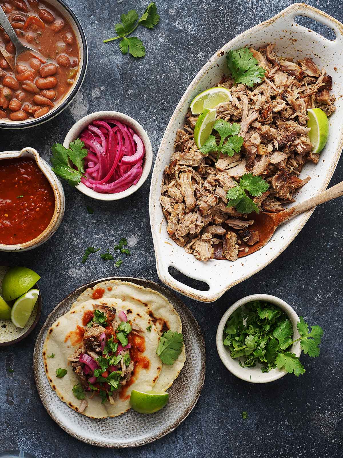 A table with pork carnitas in a plate and all garnishes on the side.
