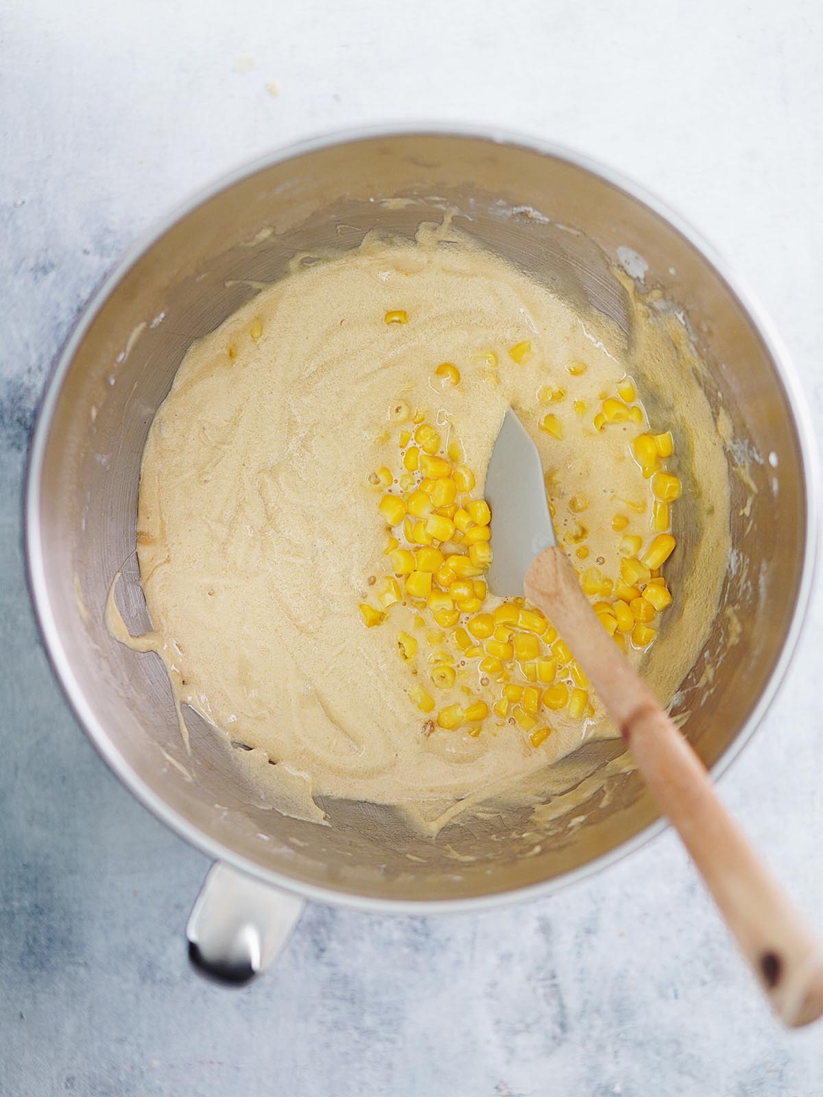 A mixing bowl with cake batter and corn kernels plus a spatula.