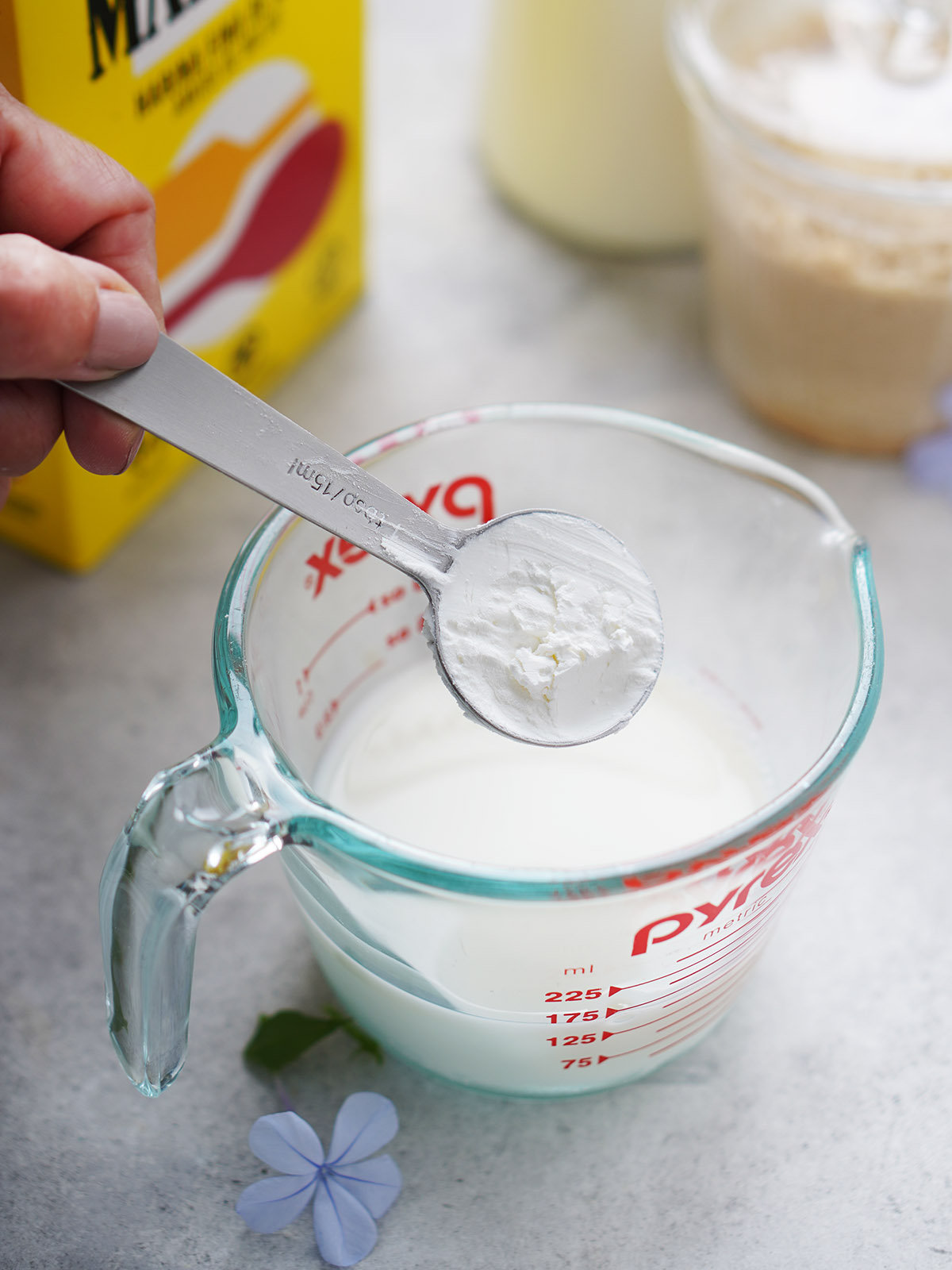 A tablespoon pouring cornstarch into a mixing cup with milk.