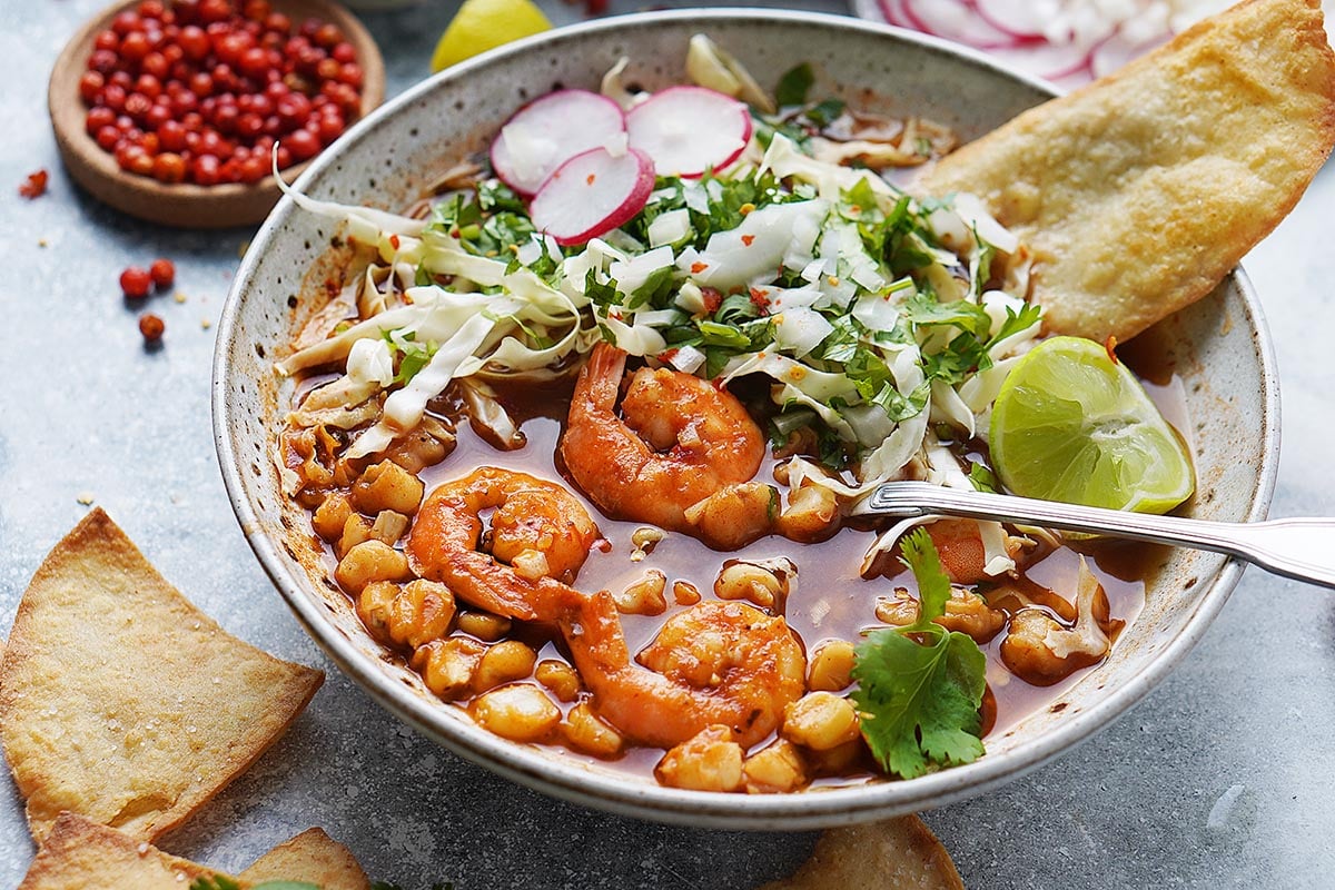 Prepared shrimp pozole in wide bowl with metal spoon.