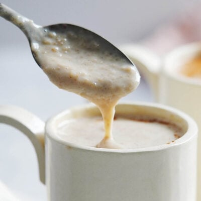 A spoon with atole de avena coming out of a mug.