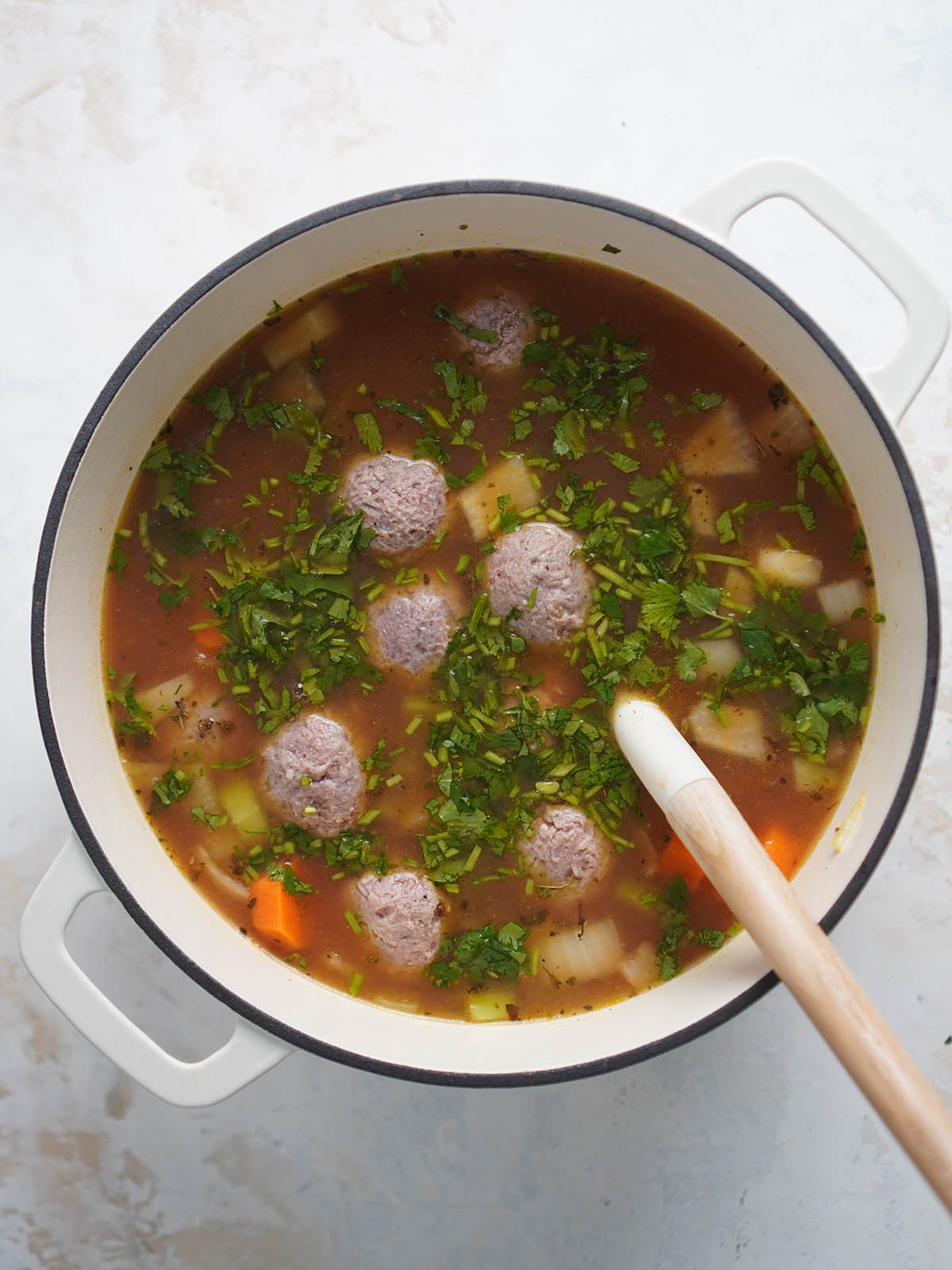 A white pot with beef meatballs in a broth and chopped cilantro.