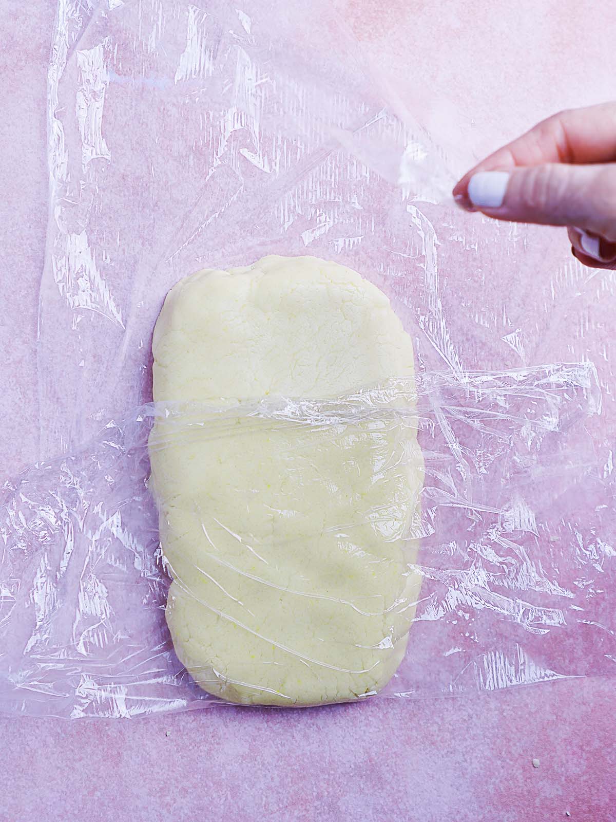 A hand placing plastic wrap over cookie dough in the shape of a rectangle.