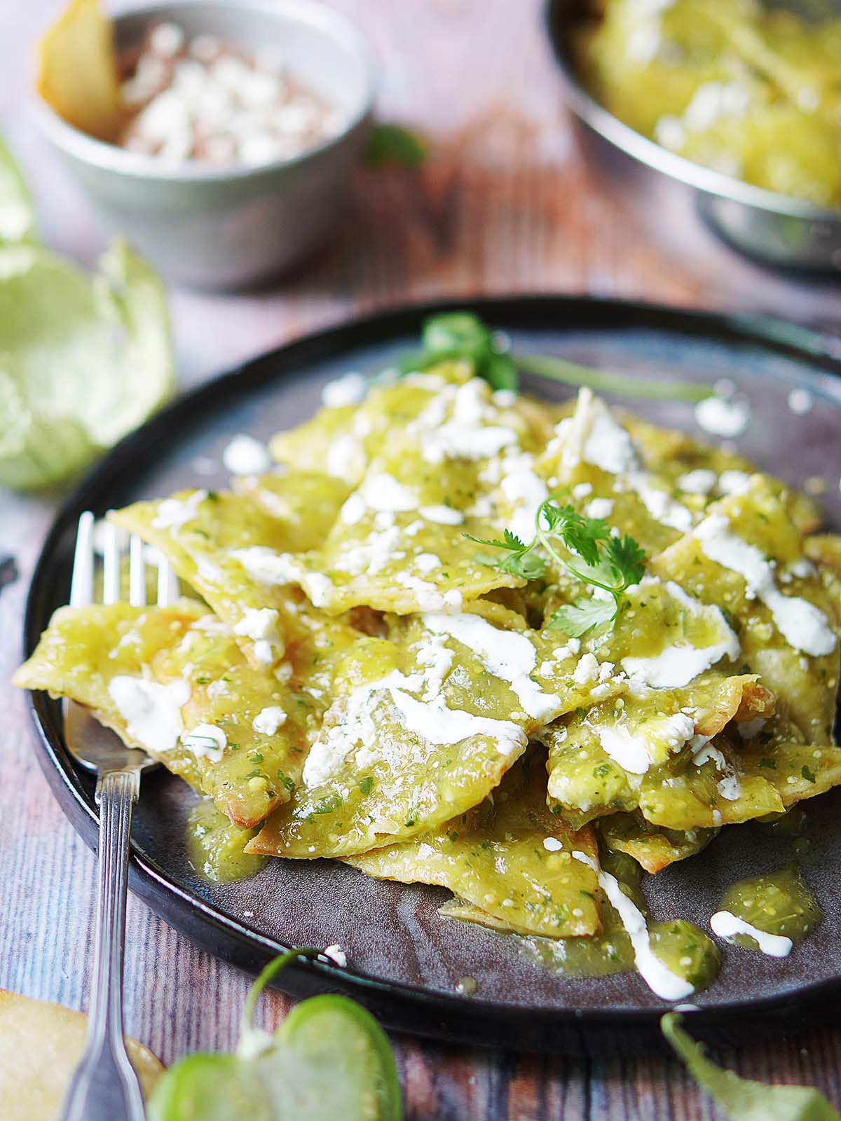 A plate with green chilaquiles drizzled with mexican crema.