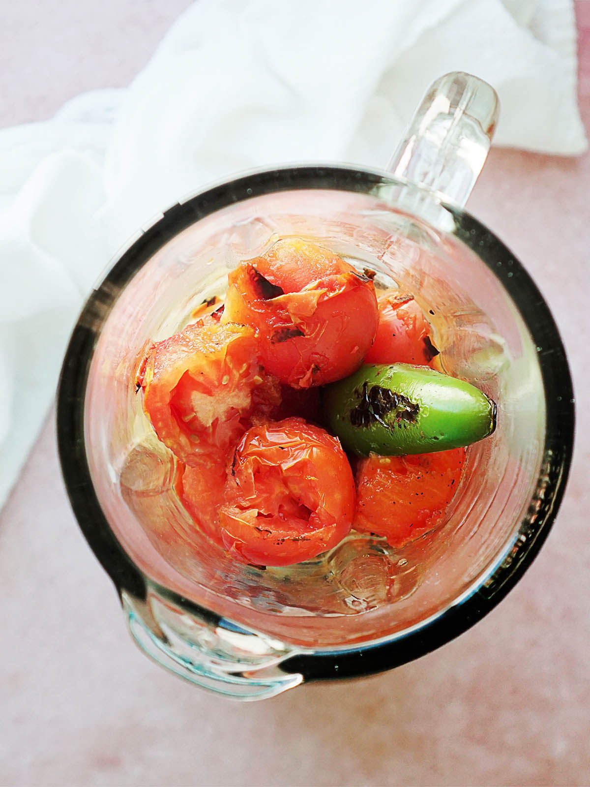 A blender's glass with the roasted tomatoes and jalapeño.