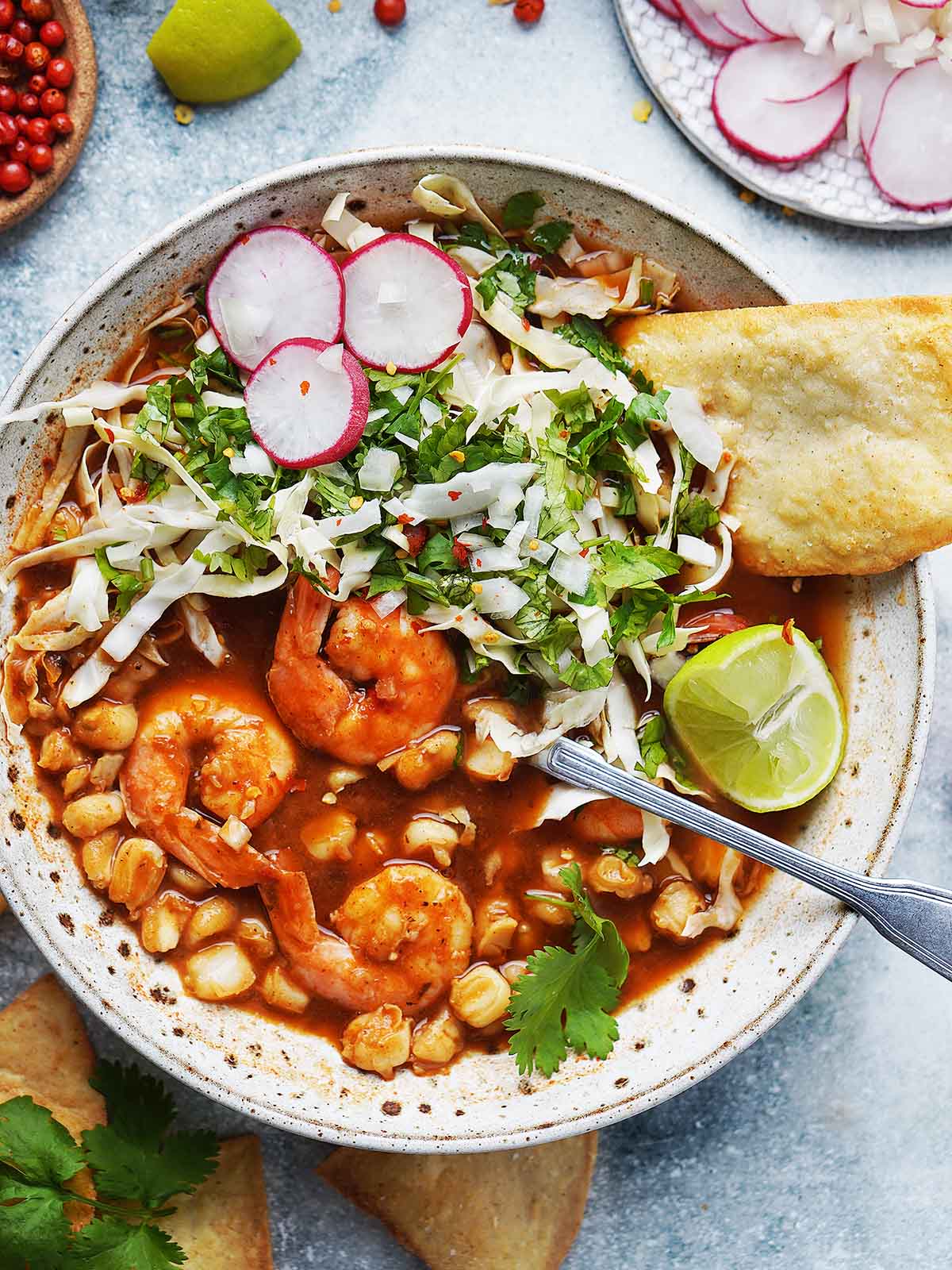 Prepared shrimp pozole in wide bowl with metal spoon.