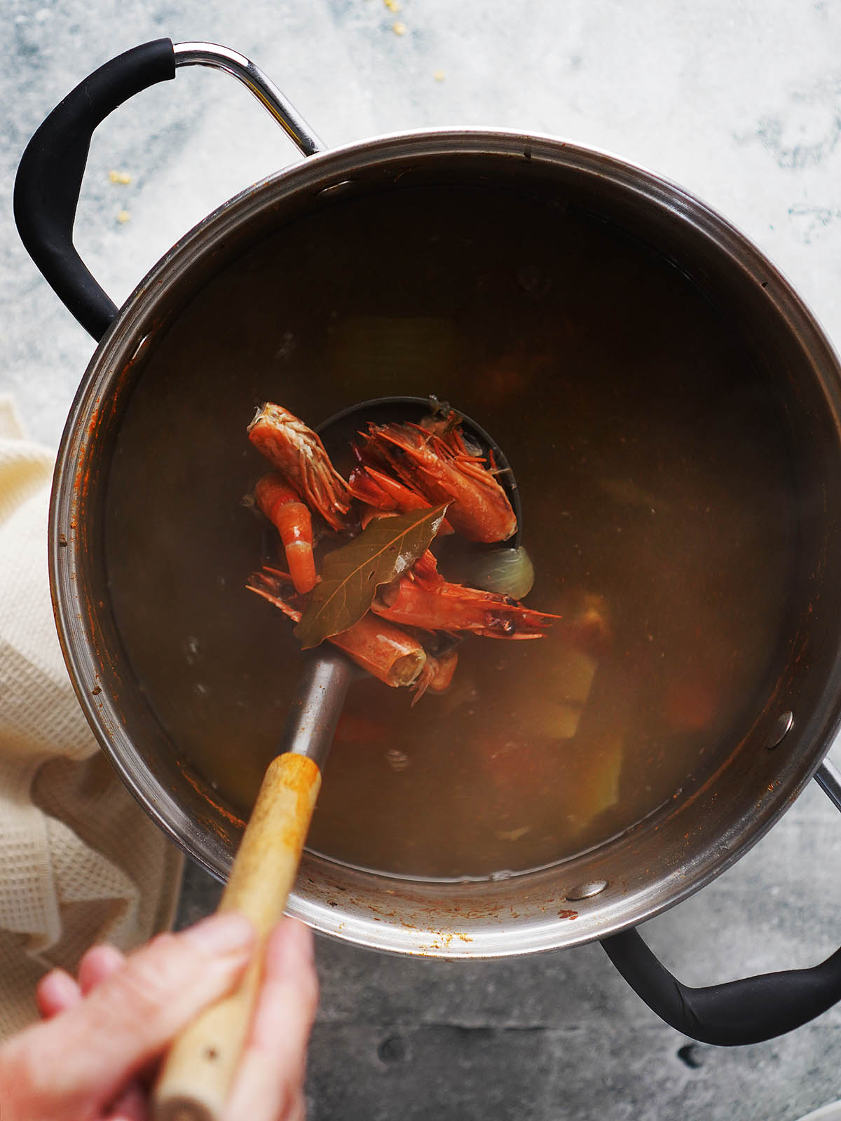 A large pot filled with stock with cooked shrimp heads and skins.
