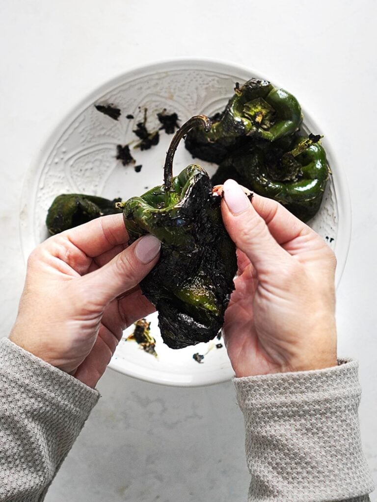 Two hands peeling the roasted poblano peppers.