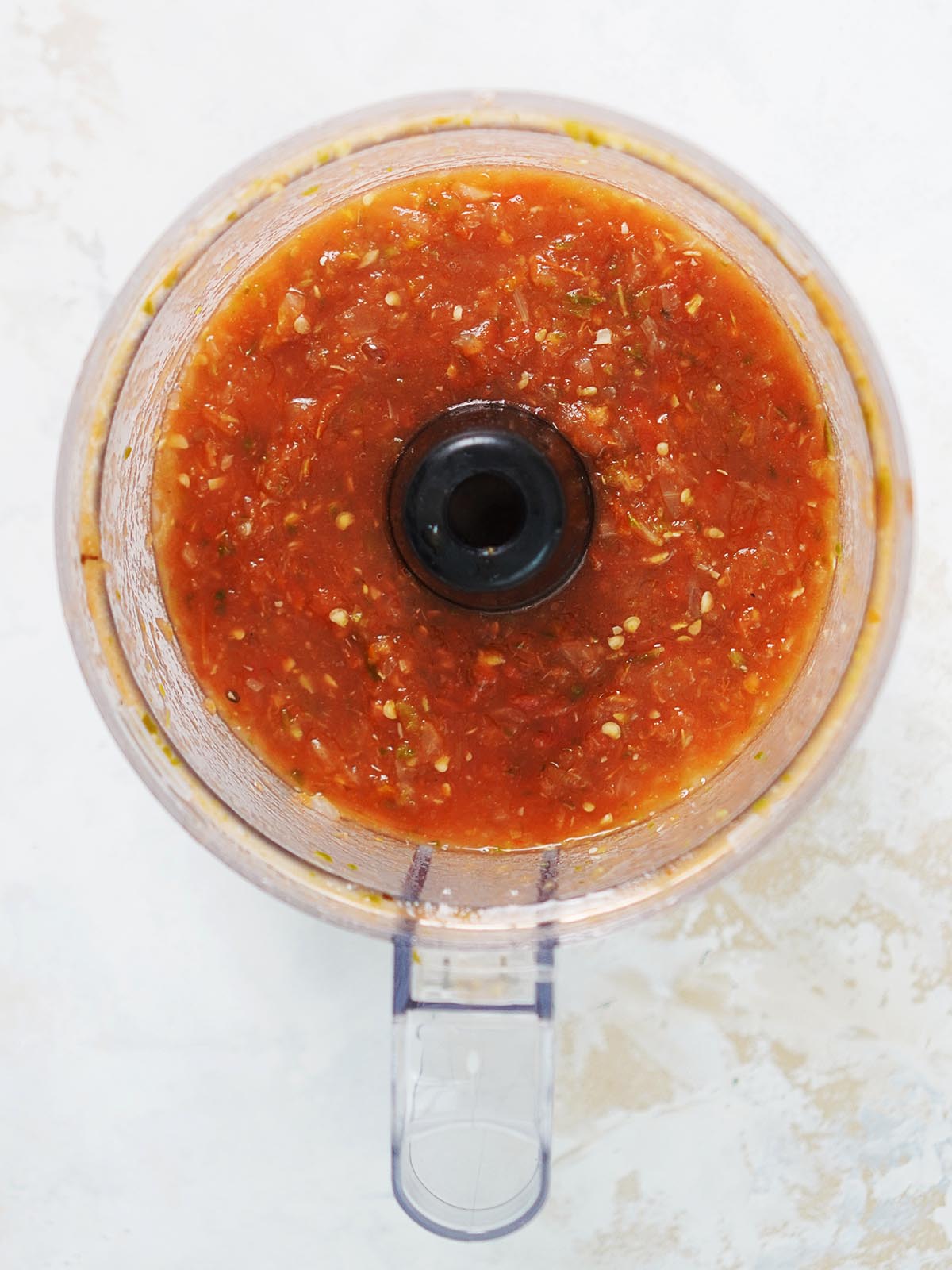 Mixed red salsa in the container of a food processor.