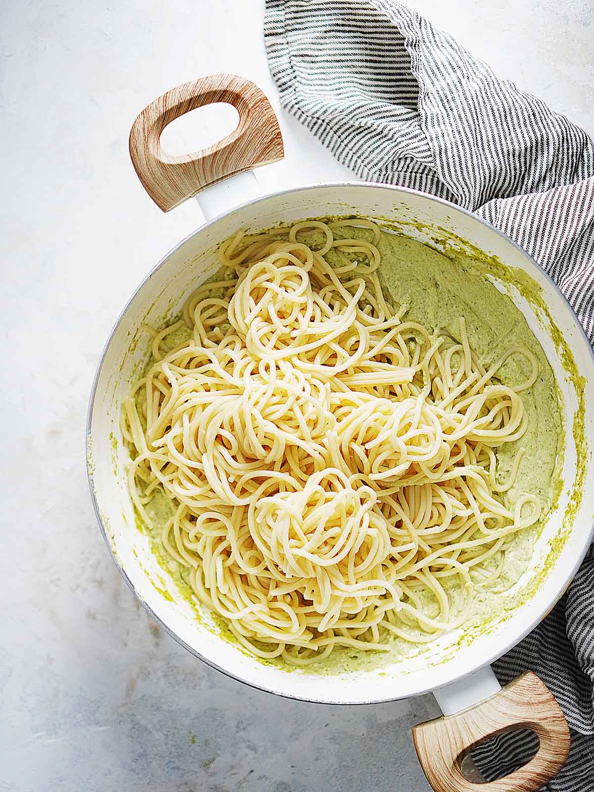 A white saucepan with green sauce and cooked spaghetti.